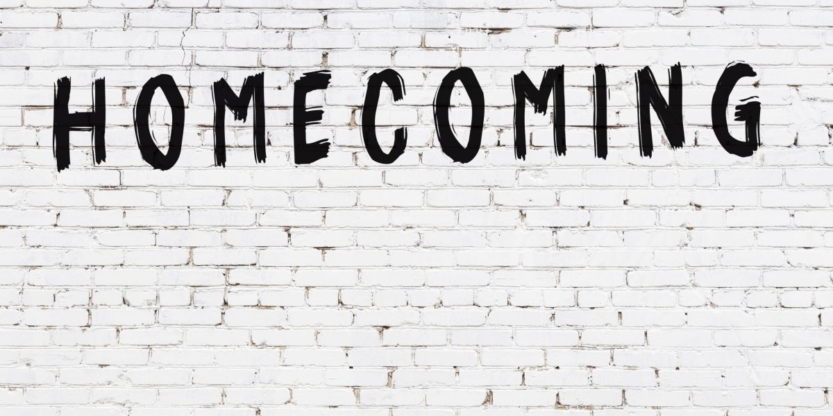 Inscription homecoming written with black paint on white brick wall.